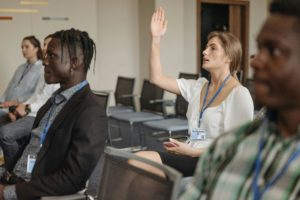 People at a professional conference. A woman has her hand up. 