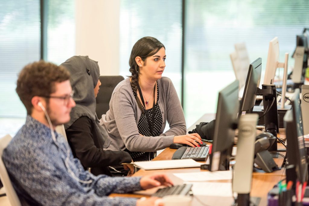 Three people at workstations with monitors in a workplace environment